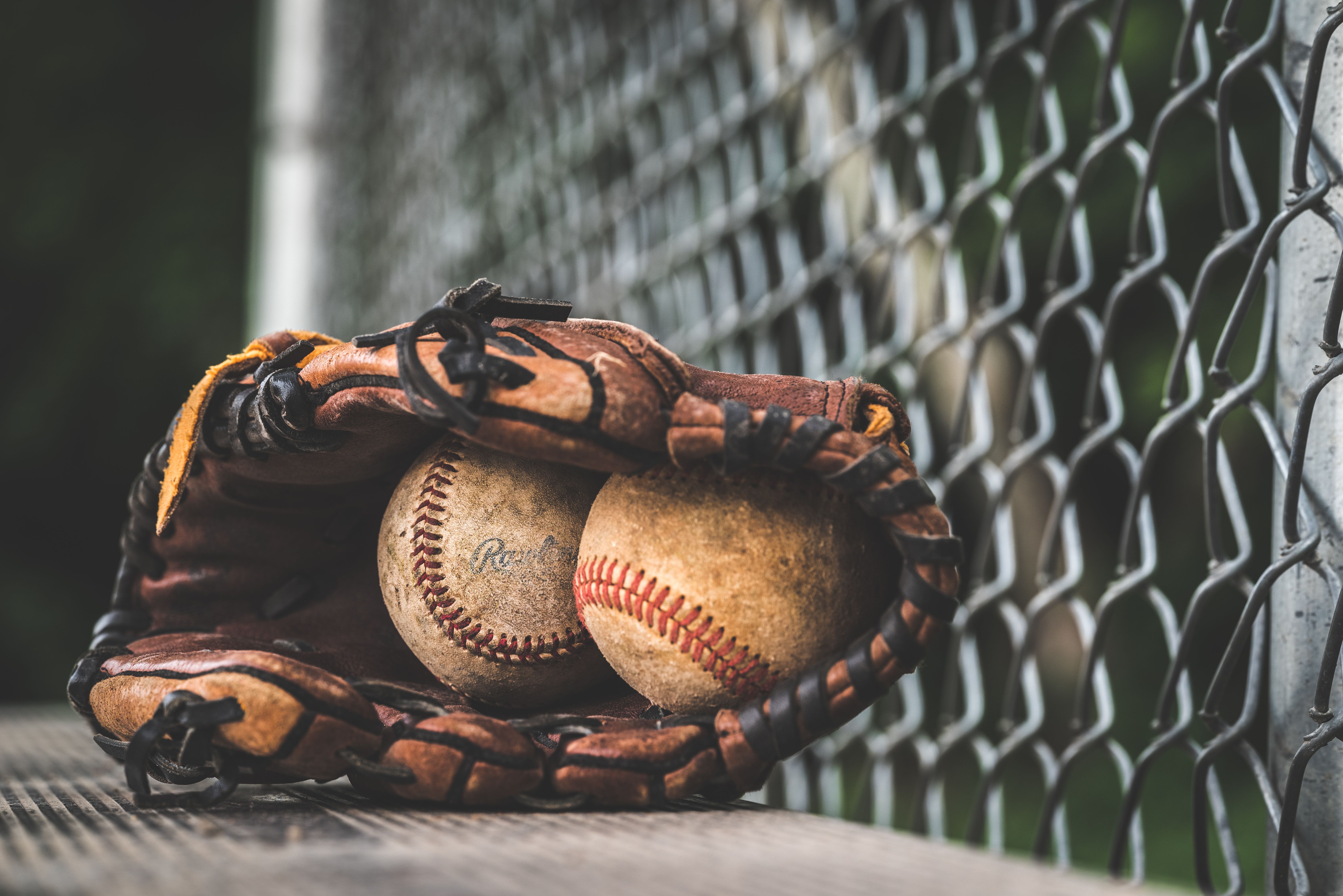 Baseball glove holding two baseballs near a chain-link fence